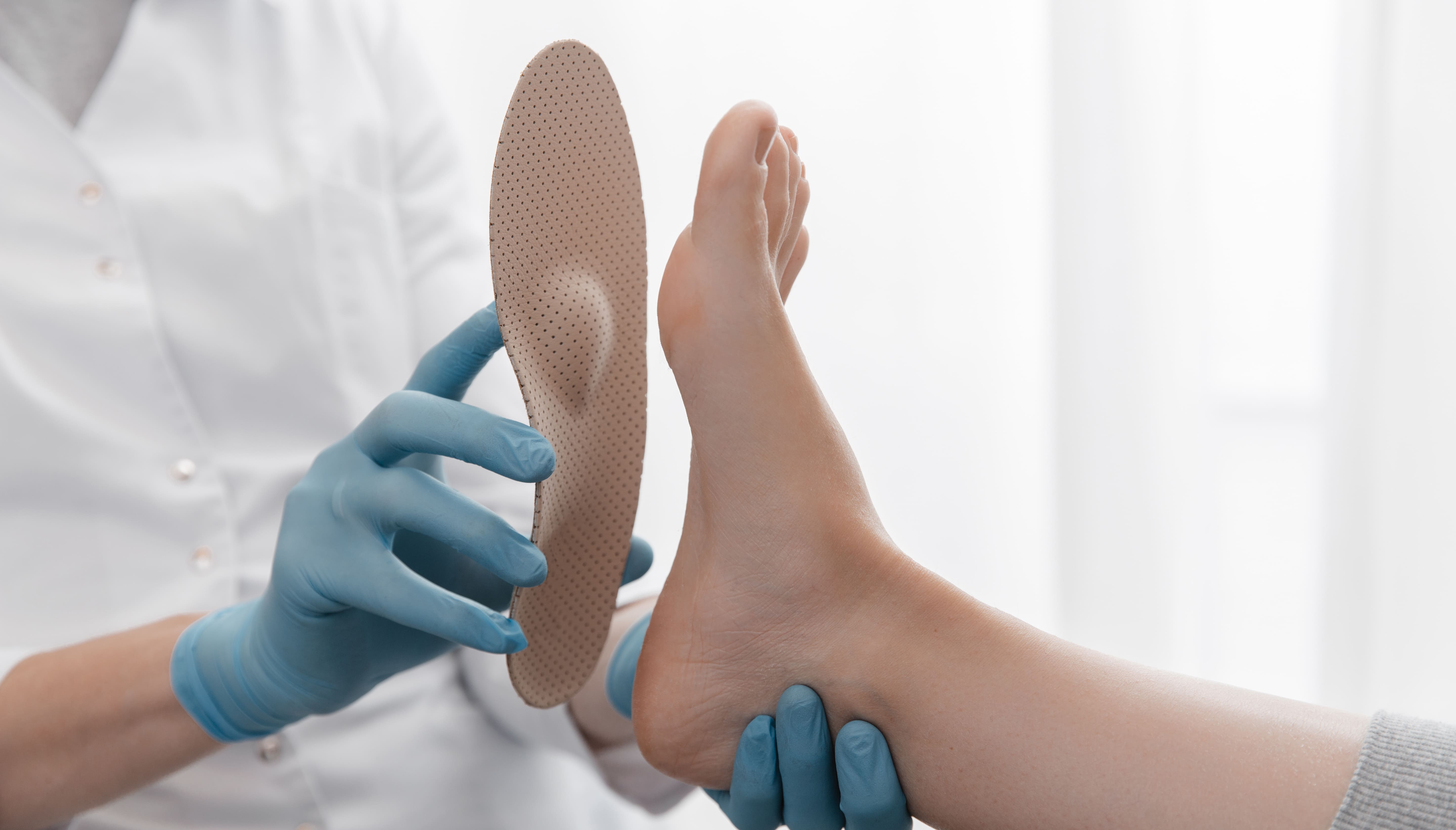 Medizinisches Personal hält eine orthopädische Schuheinlage an die Fußsohle einer Patientin.