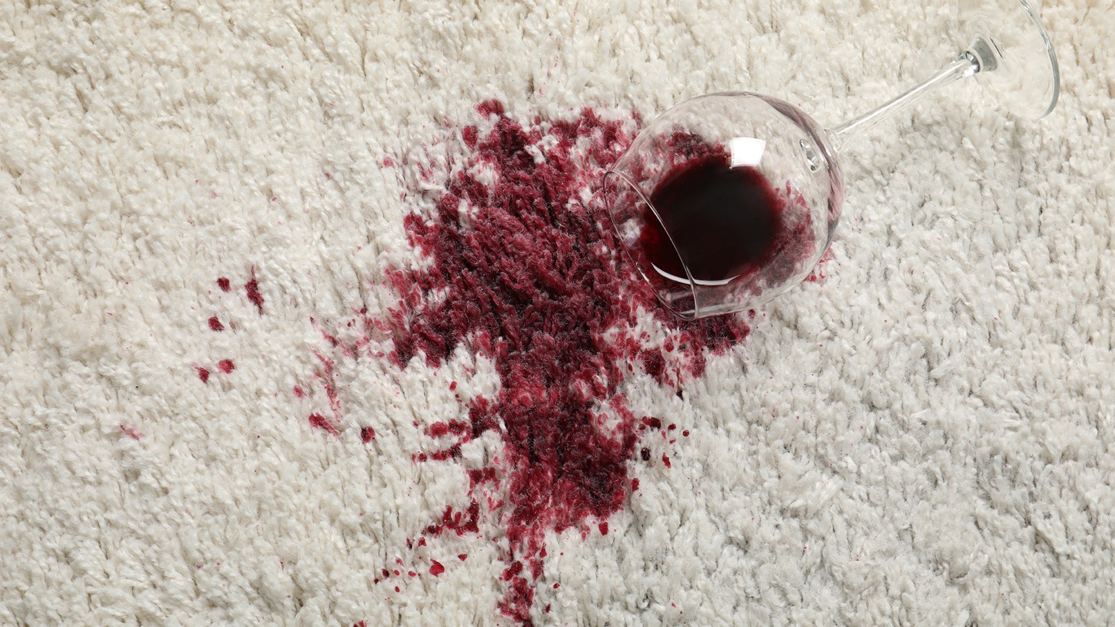Umgekipptes Glas Rotwein auf hellem Teppich